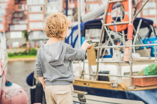 Netter blonder Junge, der Yachten und Segelboote betrachtet