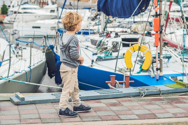 Netter blonder Junge, der Yachten und Segelboote betrachtet