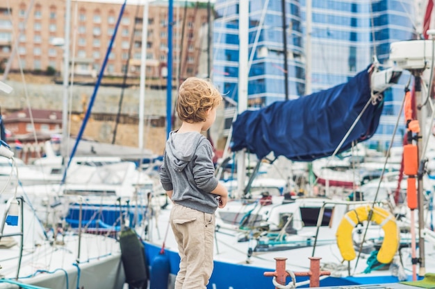 Netter blonder Junge, der Yachten und Segelboote betrachtet