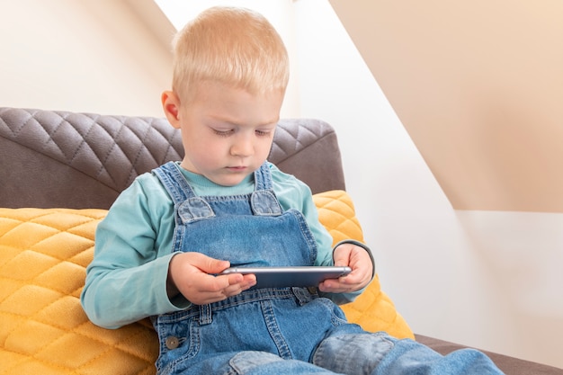 Netter blonder kleiner Junge, der Smartphone hält und Cartoons beobachtet