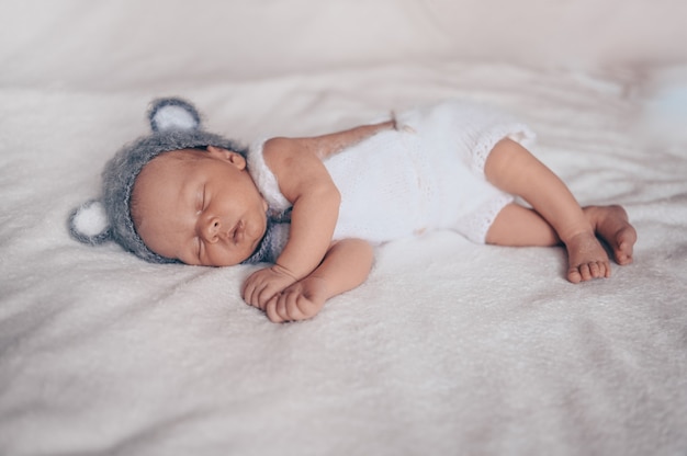 Netter emotionaler neugeborener kleiner Junge, der im Kinderbett in einem Strickanzug mit Ohren schläft.