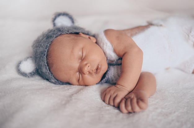 Netter emotionaler neugeborener Säuglingsbaby, das im Kinderbett in einem Strickanzug mit Ohren schläft.