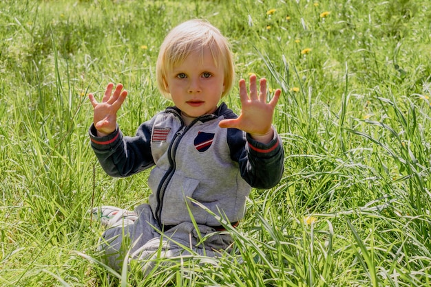 Netter entzückender kleiner kaukasischer Kleinkindjunge, der Spaß hat, auf grünem Grasrasen zu Hause im Hof zu sitzen