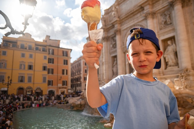 Netter fröhlicher Junge, 7 Jahre alt, isst Eisgelato in der Nähe des Trevi-Brunnens in Rom Italien