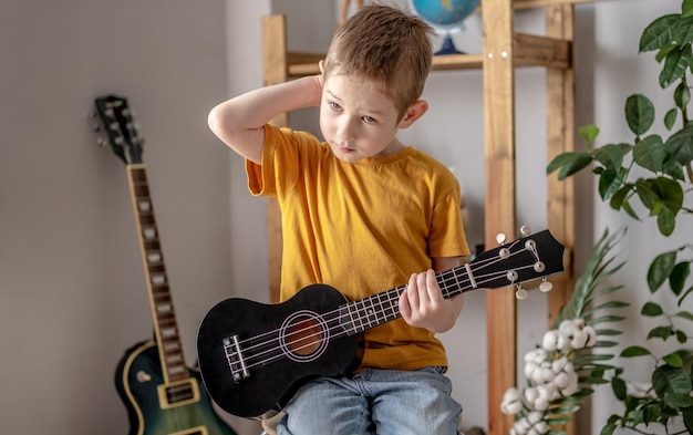 Netter fröhlicher Junge spielt Ukulele-Gitarre im Musikzimmer Fröhliches Lernen, Musikinstrumente zu spielen