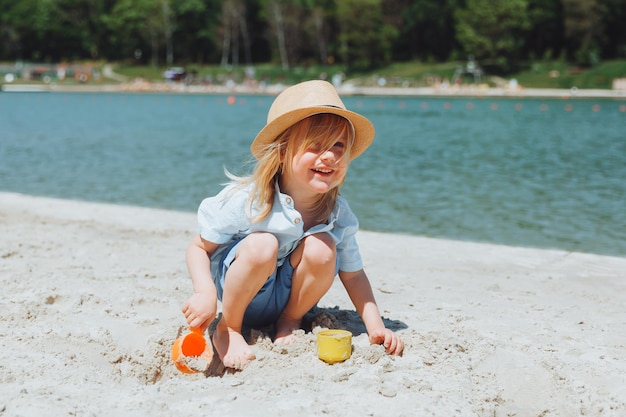 Netter glücklicher blonder Junge, der mit Strandspielzeug am sandigen Stadtstrand spielt