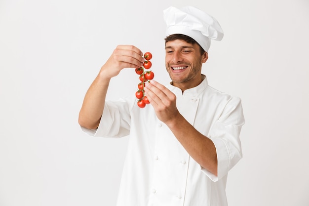 Netter glücklicher junger Koch lokalisiert auf Weiß, das Tomaten hält.