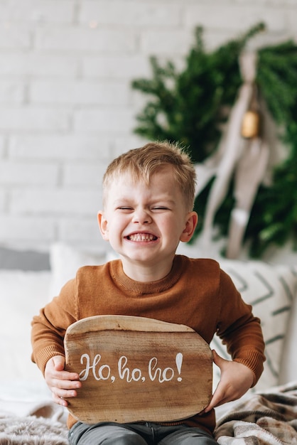 Foto netter glücklicher kaukasischer junge, der seine geschenke am weihnachtsmorgen öffnet christbaumkranz auf hintergrund kind aufgeregt und lächelnd glückliche familie urlaub zu hause öffnen von geschenken in kisten kopieren sie platz