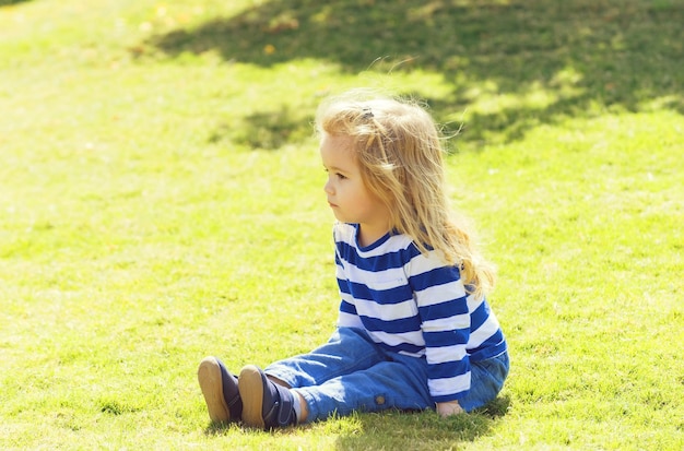 Netter glücklicher kleiner Junge, der auf grünem Gras im Park sitzt