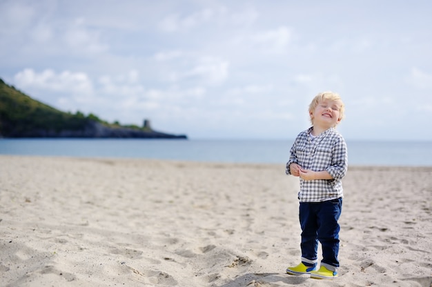 Netter glücklicher kleiner junge genießen ferien auf strand nahe tyrrhenischem meer. lustiges nettes kind, das ferien macht und sommer genießt.