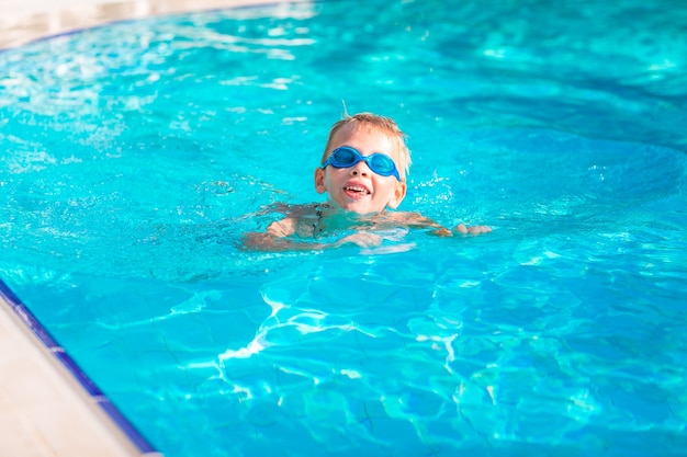 Netter glücklicher kleiner Junge in Schutzbrillen, der im Swimmingpool schwimmt und schnorchelt. Schwimmen für Kinderkonzept