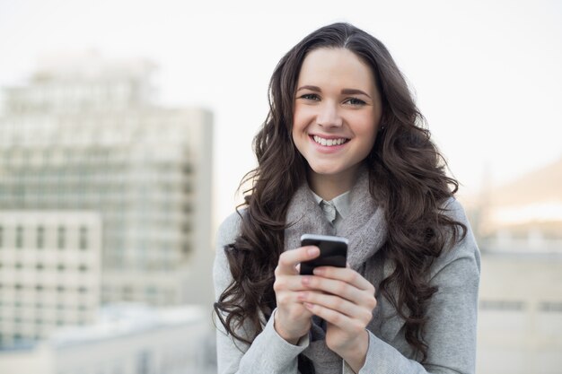 Netter hübscher Brunette, der einen Text auf ihrem Smartphone sendet