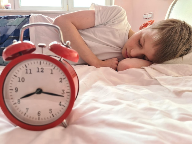 Netter jugendlich Junge mit Wecker schläft im Bett