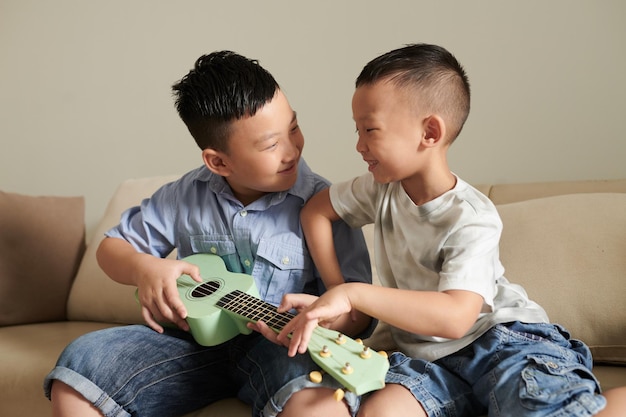 Netter jugendlicher Junge, der Bruder bittet, ihn Ukulele spielen zu lassen