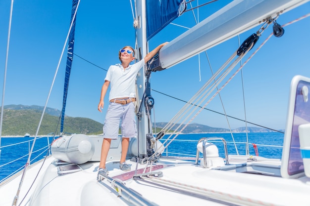 Netter Junge an Bord der Segelyacht auf Sommerkreuzfahrt. Reiseabenteuer, Segeln mit Kind im Familienurlaub. Kinderkleidung im Seemannsstil, nautische Mode.