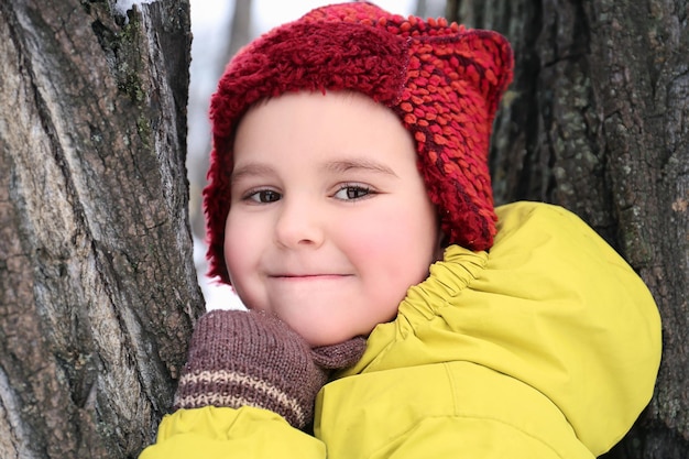 Netter Junge auf Baum im verschneiten Park im Winterurlaub