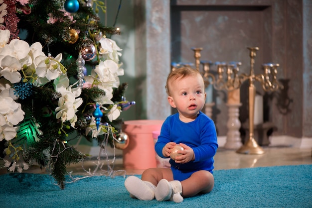 Netter Junge, der auf dem Teppich nahe Weihnachtsbaum sitzt