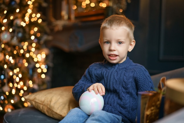 Netter Junge, der auf der Couch im Hintergrund des Weihnachtsbaums sitzt.