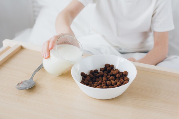 Netter Junge, der die Frühstücksschokoladenbälle sitzen im Bett mit weißer Bettwäsche isst