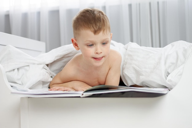 Netter junge, der ein buch in einem weißen bett liest