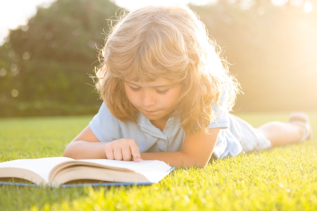 Netter Junge, der ein Buch liest, das auf Gras legt. Kind, das ein Buch im Sommerpark liest