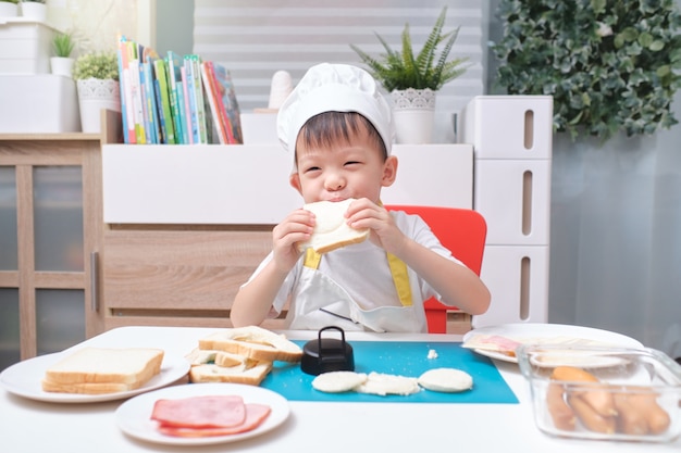 Netter Junge, der eine Kochmütze und eine Schürze trägt, die Sandwiches vorbereiten