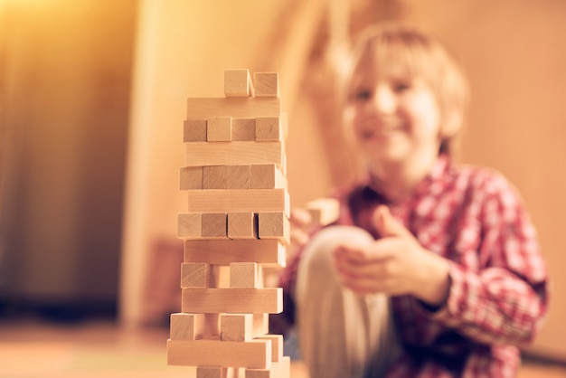 Netter Junge der Vorschule, der in einem Tischspiel mit Holzklötzen zu Hause spielt