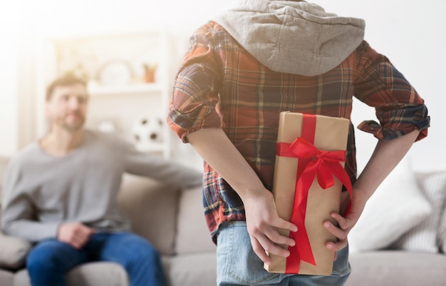 Netter Junge, der zu Hause Geschenk für Vater hinter seinem Rücken hält, Nahaufnahme