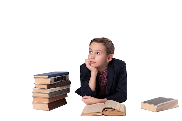 Netter Junge im Anzug liegt und träumt auf weißem Hintergrund. ein Stapel Bücher.