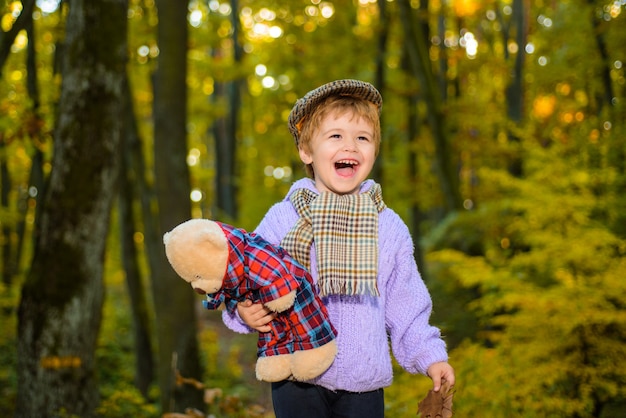 Netter Junge im Herbstpark Herbstkind kleiner Junge spielt mit Teddybär im Parkherbstzeit kleiner Junge