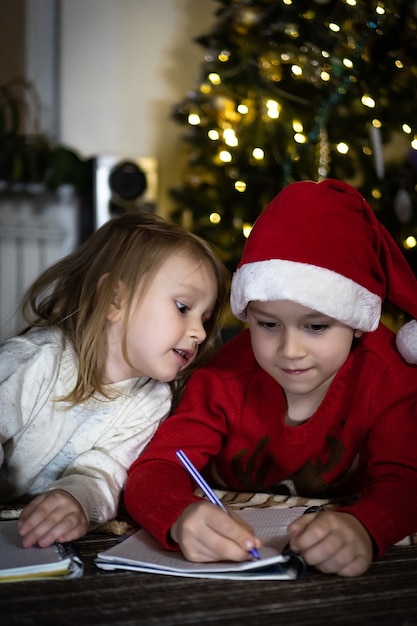 Netter Junge im roten Pullover und in der roten Weihnachtsmütze schreibt einen Brief an den Weihnachtsmann