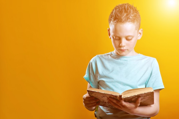 Netter Junge in einem hellen T-Shirt, das ein Buch auf gefärbt hält