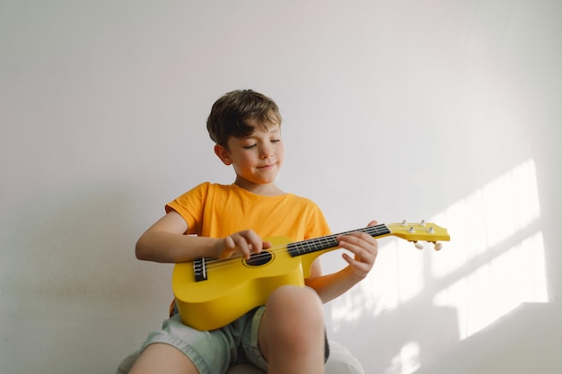 Foto netter junge lernt zu hause die gelbe ukulele-gitarre zu spielen