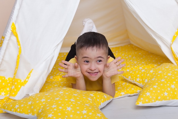 Netter Junge mit Down-Syndrom, der in einer gelben Hütte sitzt