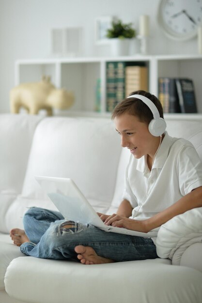 Netter Junge mit Kopfhörern, wenn er zu Hause einen Laptop benutzt