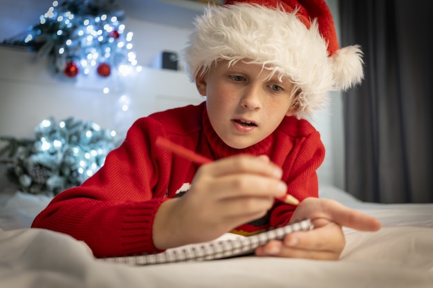 Netter Junge schreibt Brief an den Weihnachtsmann, der sich auf das Weihnachtswunder-Wunschliste-Kind-Liegen vorbereitet