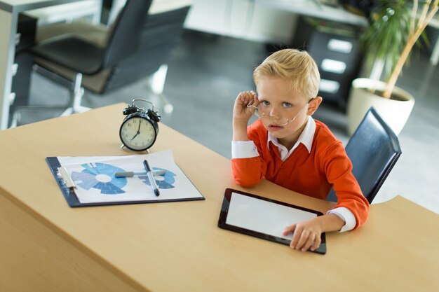 Netter Junge sitzen am Schreibtisch im Büro und benutzt Tablet-PC