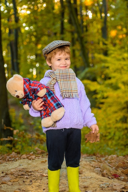 Netter junge über herbsthintergrund kleiner junge, der im park süßer junge mit teddybär im herbst spielt