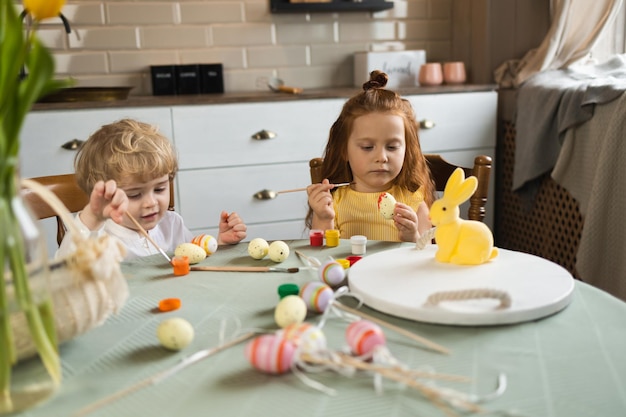 Netter Junge und Mädchen sitzen in der Küche und malen Feiertagseier