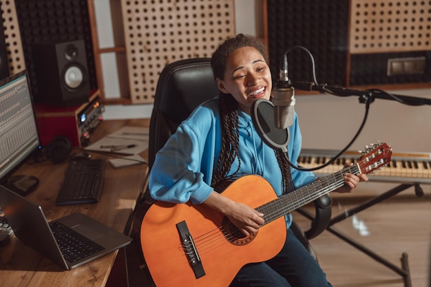 Netter junger afrikanischer Musiker, der ins Mikrofon singt, während er ein neues Lied aufführt und Gitarre spielt