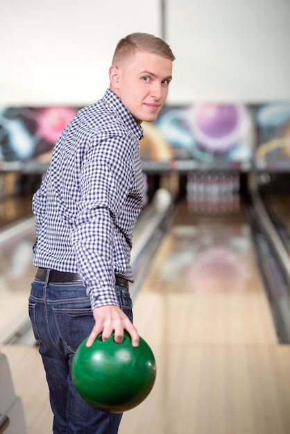 Netter junger Mann, der Bowlingspiel spielt.