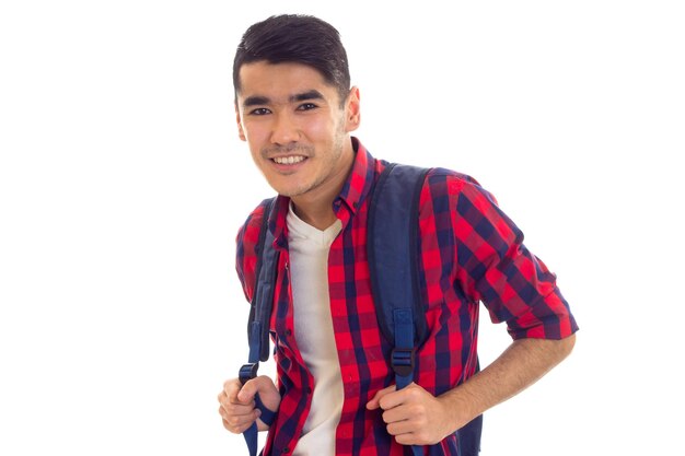 Netter junger Mann mit schwarzen Haaren in weißem T-Shirt und rot kariertem Hemd mit blauem Rucksack
