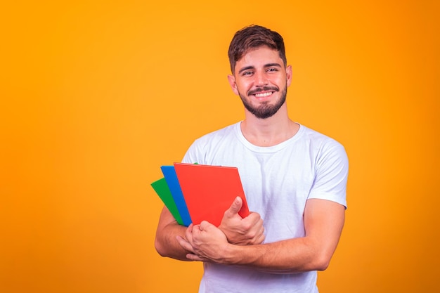 Netter junger Studentenjunge, der Bücher auf gelbem Hintergrund hält.