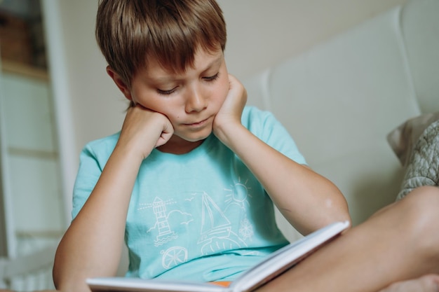 Netter kaukasischer Junge, der ein Buch liest, das auf dem Bett im Schlafzimmer der Eltern sitzt