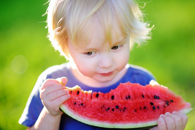 Netter kaukasischer kleiner Junge mit den blonden Haaren frische Wassermelone draußen essend