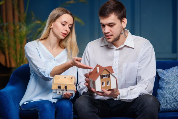 Netter kaukasischer Mann und Frau, die zwei Modell des 3d Maket des Hauses diskutieren.