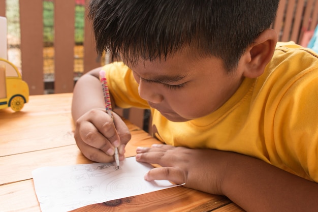 Netter Kinderasiatischer kleiner Junge, der Hausarbeit auf Tabelle tut