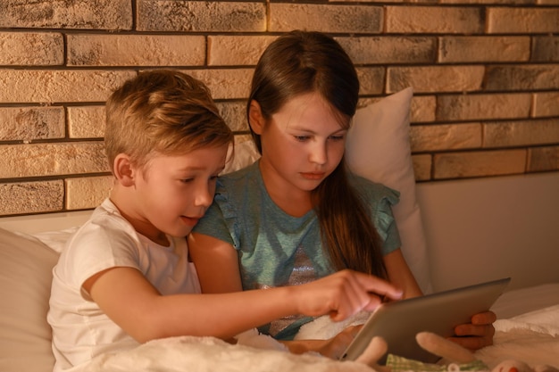Netter kleiner Bruder und Schwester, die abends Gute-Nacht-Geschichte vom Tablet-Computer lesen