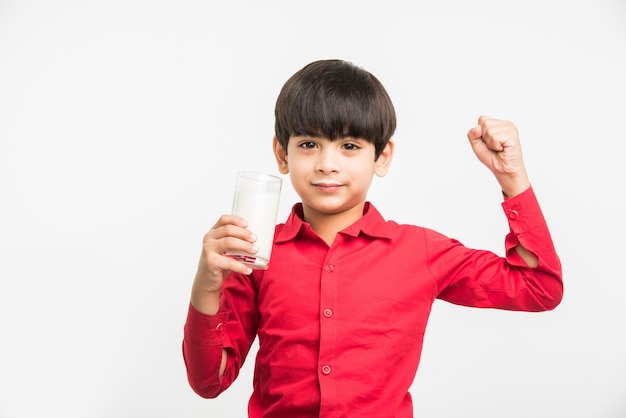 Netter kleiner indischer oder asiatischer verspielter Junge, der ein Glas Milch hält oder trinkt, isoliert auf weißem Hintergrund