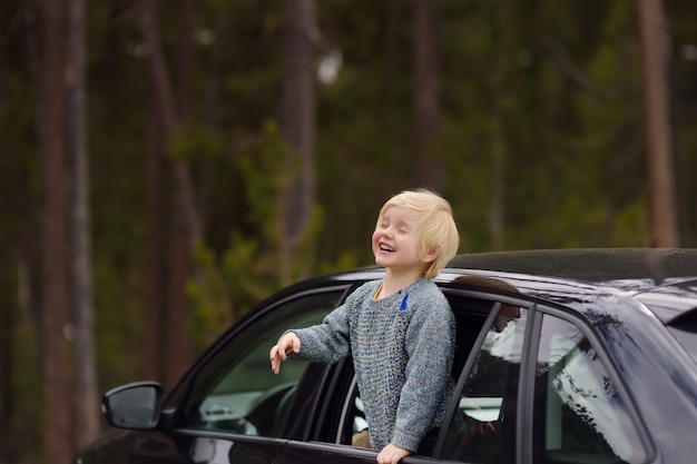 Netter kleiner Junge bereit zu einem Roadtrip oder zu einer Reise. Familienauto mit Kindern.